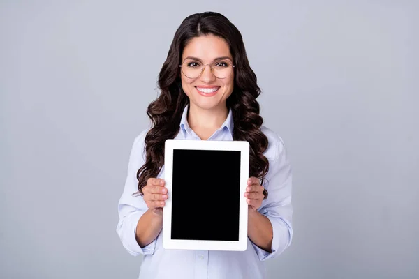 Foto de positivo feliz dama mantenga tableta pantalla táctil espacio vacío desgaste especificaciones camisa azul aislado gris color fondo — Foto de Stock