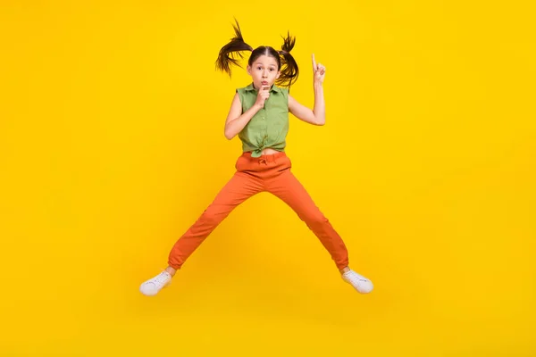 Foto de estudante sério brilhante menina usar camisa verde sorrindo pulando lábios de dedo alto pedindo para manter o silêncio isolado cor amarela fundo — Fotografia de Stock