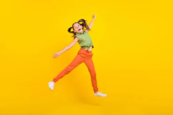 Foto de estudante bonita despreocupada usar camisa verde sorrindo pulando lados do braço alto isolado cor amarela fundo — Fotografia de Stock