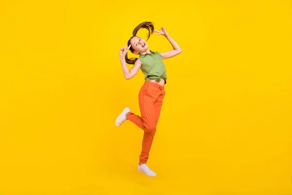 Foto de encantadora menina pré-adolescente alegre vestido top verde saltando alto mostrando dois v-sinais sorrindo isolado cor amarela fundo — Fotografia de Stock