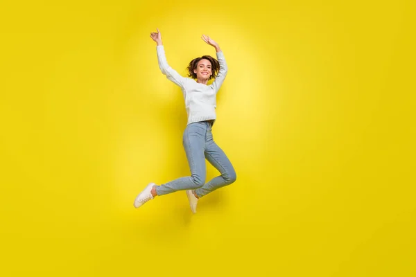 无忧无虑的女士跳跃的照片举臂穿蓝色毛衣牛仔裤运动鞋孤立的黄色背景 — 图库照片