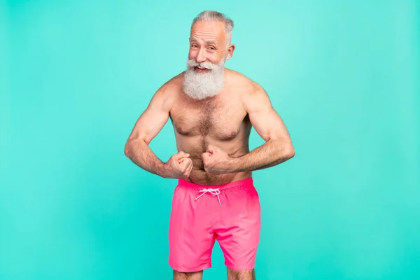 Photo of flirty retired old man show strength arms muscles wear pink shorts isolated teal color background.