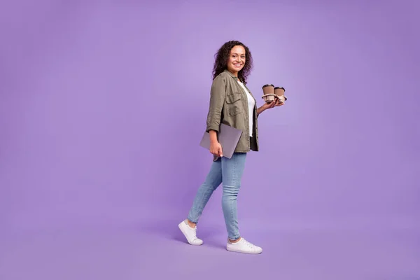 フルボディ写真のブルネットの髪トレンディなアフロアメリカ人女性歩くホールドコーヒーノートパソコン孤立した上紫の色の背景 — ストック写真