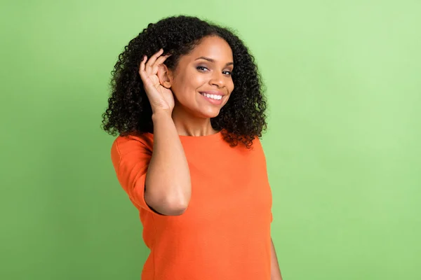 Photo of young african woman happy positive smile hand near ear listen news gossip isolated over green color background.