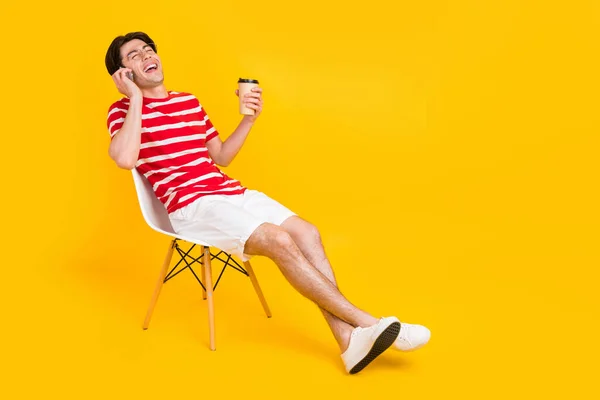 幸せな正明るい男トーク電話ホールドコーヒー椅子は黄色の背景に隔離された — ストック写真