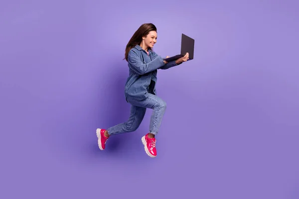 Full body profile portrait of active cheerful girl jump hurry rush use netbook isolated on purple color background.