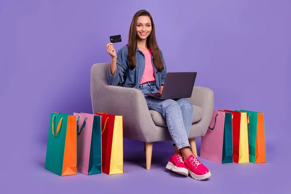 Full size photo of cheerful attractive lady sit chair use netbook hold debit credit card isolated on violet color background.