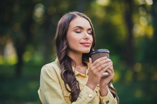 Portrait of attractive cheery calm peaceful long-haired girl enjoying drinking espresso in forest outdoors.