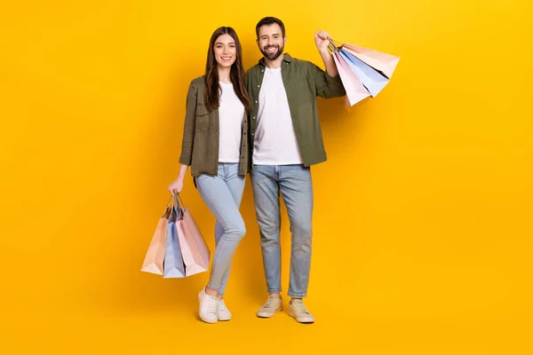 Full body photo of lovely couple hold shopping bags with stylish clothes isolated on yellow color background.