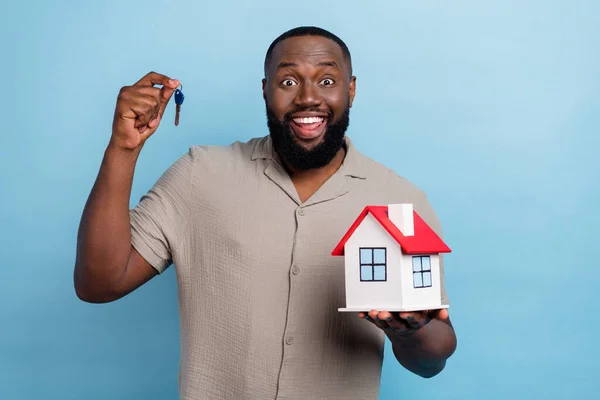 Portrait of positive satisfied person hold demonstrate small house key isolated on blue color background.
