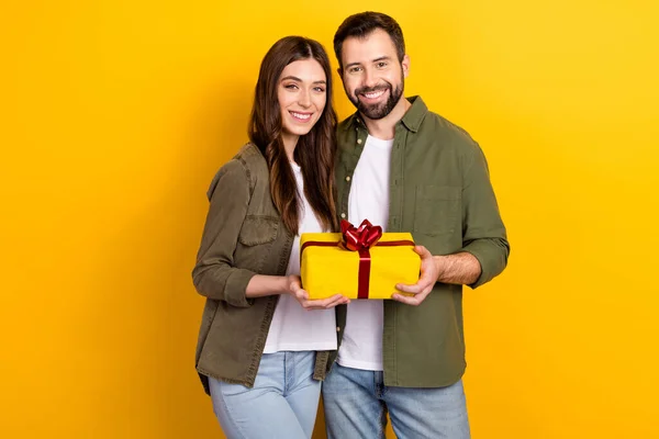 Portrait of two cheerful peaceful people hold giftbox look camera isolated on yellow color background.