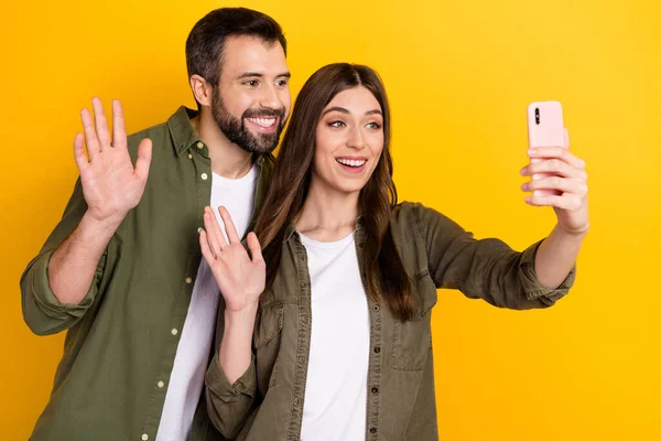 stock image Portrait of attractive cheerful couple using device waving hi hello making selfie isolated over bright yellow color background.