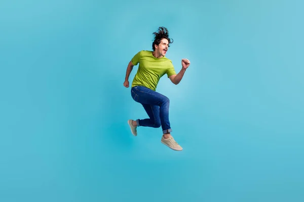 Full length photo of attractive purposeful guy dressed green t-shirt jumping high running fast isolated blue color background.