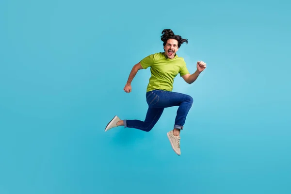 Full length photo of purposeful funky guy dressed green t-shirt jumping high running fast isolated blue color background.