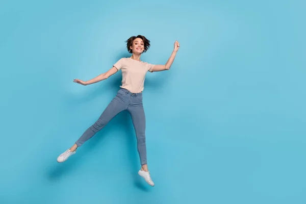 Full length photo of sweet pretty woman wear beige t-shirt jumping high empty space isolated blue color background.