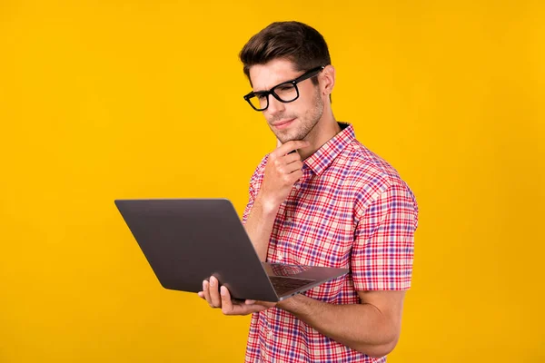Portrait of attractive trendy focused guy geek hacker using laptop reading report isolated over bright yellow color background.