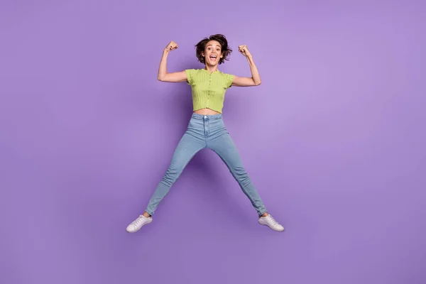 魅力的な強い若い女性の写真を着て緑のTシャツ筋肉を示すジャンプ高孤立紫色の背景 — ストック写真
