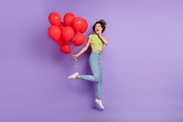 Photo of beautiful attractive excited emotion young woman dressed green t-shirt holding red air balls jumping high isolated purple color background.