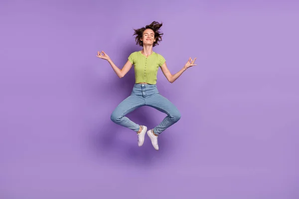 平和的な美しい若い女性の写真を着て緑のTシャツ笑顔ジャンプ高練習ヨガ孤立紫色の背景 — ストック写真
