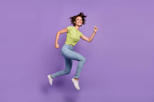 漂亮漂亮的年轻女士穿着绿色T恤 微笑着跳高跑高跑高的紫色背景的照片 — 图库照片