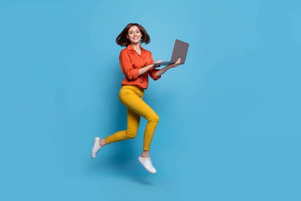 在明亮的蓝色背景下 用笔记本电脑从全长体形上看到迷人的欢快 时髦的女孩跳起来 — 图库照片