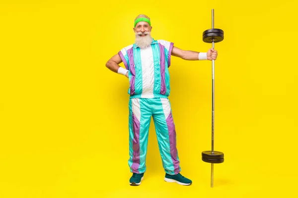Full body photo of cheerful aged person put hand waist hold barbell isolated on yellow color background.