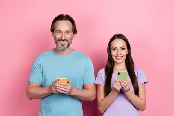 Photo of two peaceful cheerful people hold use telephone toothy smile isolated on pink color background.