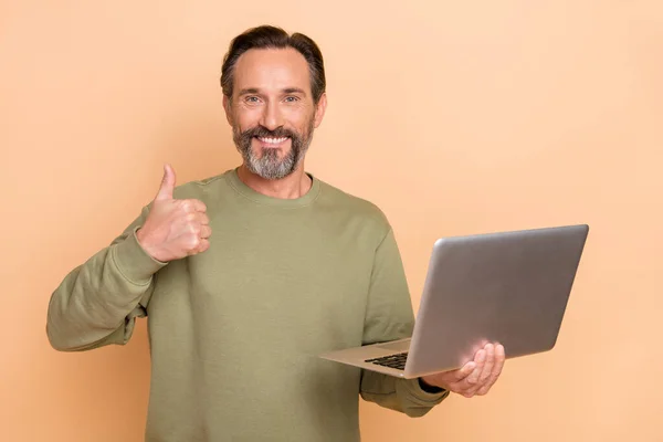 魅力的な陽気な成功した男の肖像画を使用してノートパソコンを示す親指の広告はベージュのパステルカラーの背景に隔離 — ストック写真