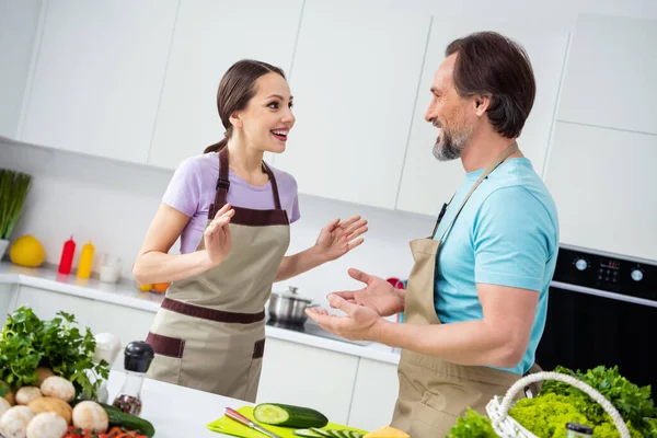 Photo of two friendly people speak conversation cooking together kitchen indoors.