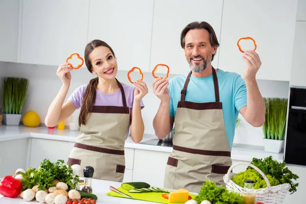 Photo of two cheerful friendly people hold paprika pepper fresh slices kitchen indoors.