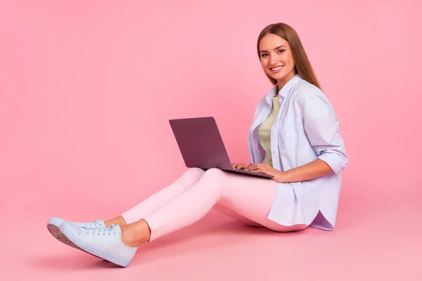 Full body portrait of pretty positive lady sitting floor use wireless netbook write email isolated on pink color background.