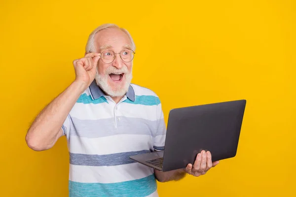 Portrait of attractive amazed cheerful grey haired man using laptop advert it isolated over bright yellow color background.