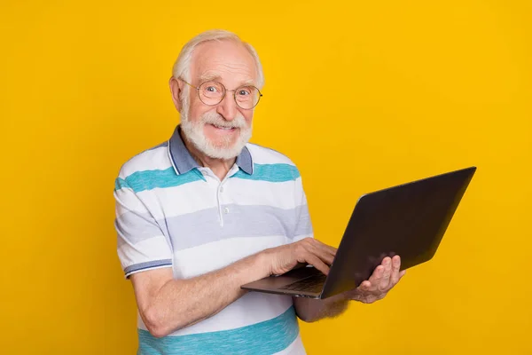 Portrait of attractive cheerful grey haired man using laptop watching movie film isolated over bright yellow color background.