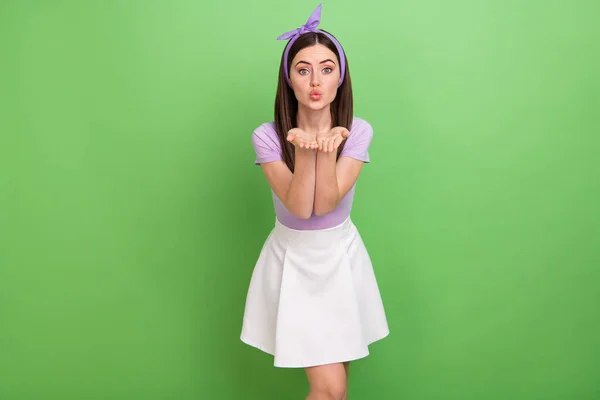 Photo of sweet adorable lady dressed purple t-shirt hairband sending you arms kiss isolated green color background.