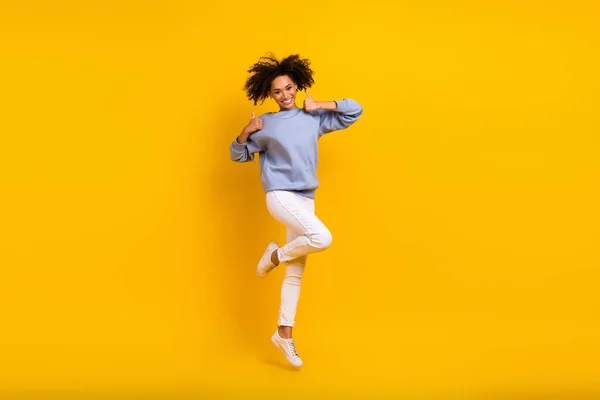 소녀가 점프하는 사진은 노란색 배경에 외따로 떨어져 엄지손가락을 — 스톡 사진