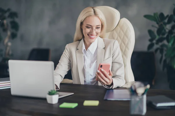 Portrait of smart positive lady sitting chair use telephone read email modern office building indoors.