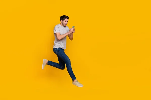 用在鲜活的黄色背景上独立运行的装置拍摄的有吸引力的快乐男人跳跃的全长体形图像 — 图库照片