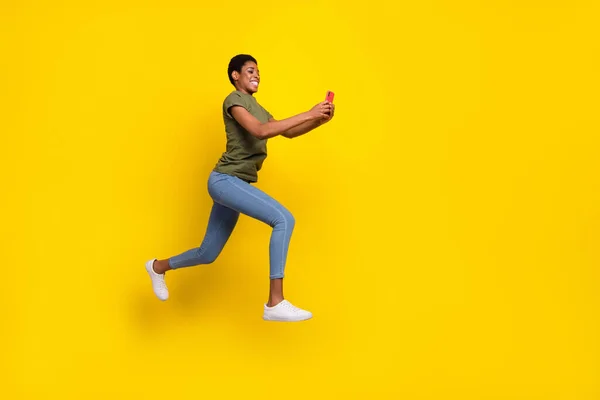 Full size portrait of crazy sporty person hold telephone jump rush fast isolated on yellow color background.