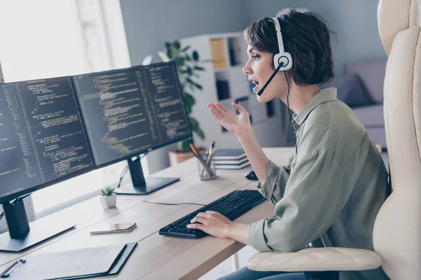 Profile photo of skilled pc expert sitting chair speak communicate clients headphones look screen workplace indoors.