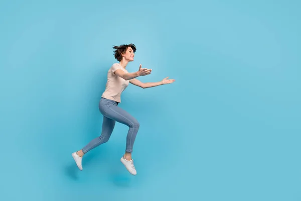 Full length photo of sweet funny lady dressed beige t-shirt jumping high catching arms empty space isolated blue color background.