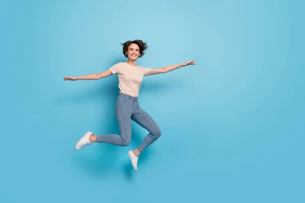 Full length photo of funny shiny lady dressed beige t-shirt jumping arms sides empty space isolated blue color background.