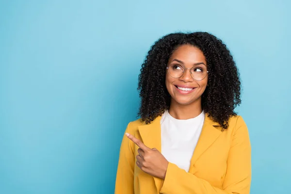 Photo of young black woman happy positive smile indicate finger empty space choose promo isolated over blue color background.