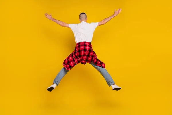 Full length photo of young man jump up raise hands star shape checkered shirt tied on waist isolated on yellow color background.