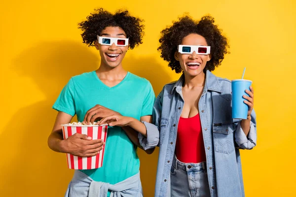 Photo of amazed dark skin people couple relationship movie glasses pop corn drink isolated on yellow color background.
