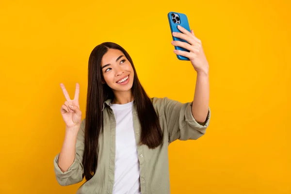Photo of young pretty cute girl take selfie showing v sign make new post for her blog isolated on yellow color background.