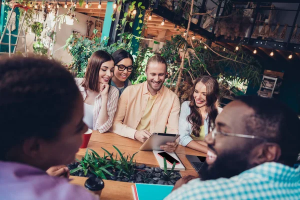 Portrait of friendly satisfied students company sitting cafe use tablet chatting conversation indoors.