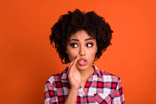 Photo of young nervous person hand near mouth tell look empty space isolated on orange color background.