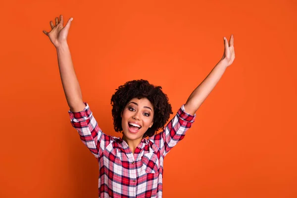 Photo of adorable excited lady dressed checkered shirt rising arms smiling isolated orange color background.