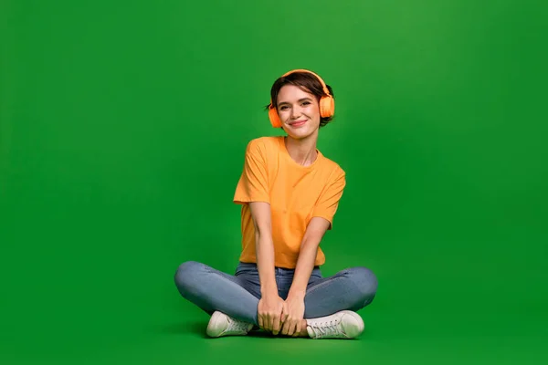 Full length photo of charming peaceful girl sit floor enjoy new playlist isolated on green color background.