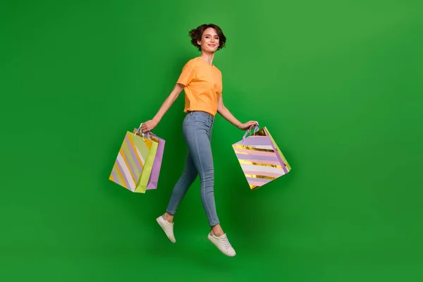 Full size profile photo of excited carefree girl jump hands hold packages isolated on green color background.